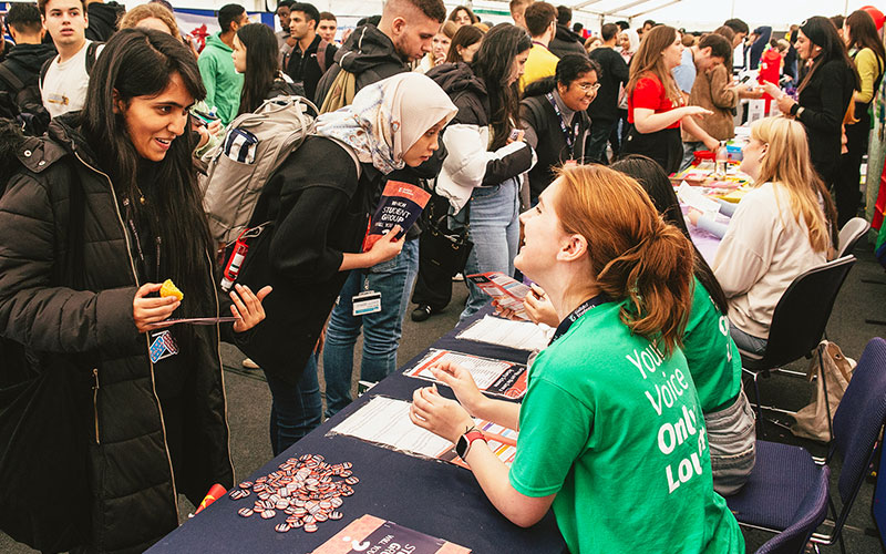 a photo of a student staff member talking to students at societies fair